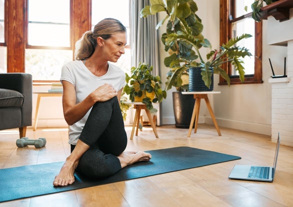 A woman performing yoga in front of a laptop